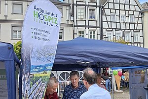 Menschen an einem Informationsstand mit Fahne des Ambulanten Hospiz Neuwied vor Fachwerkhäusern auf einem Marktplatz